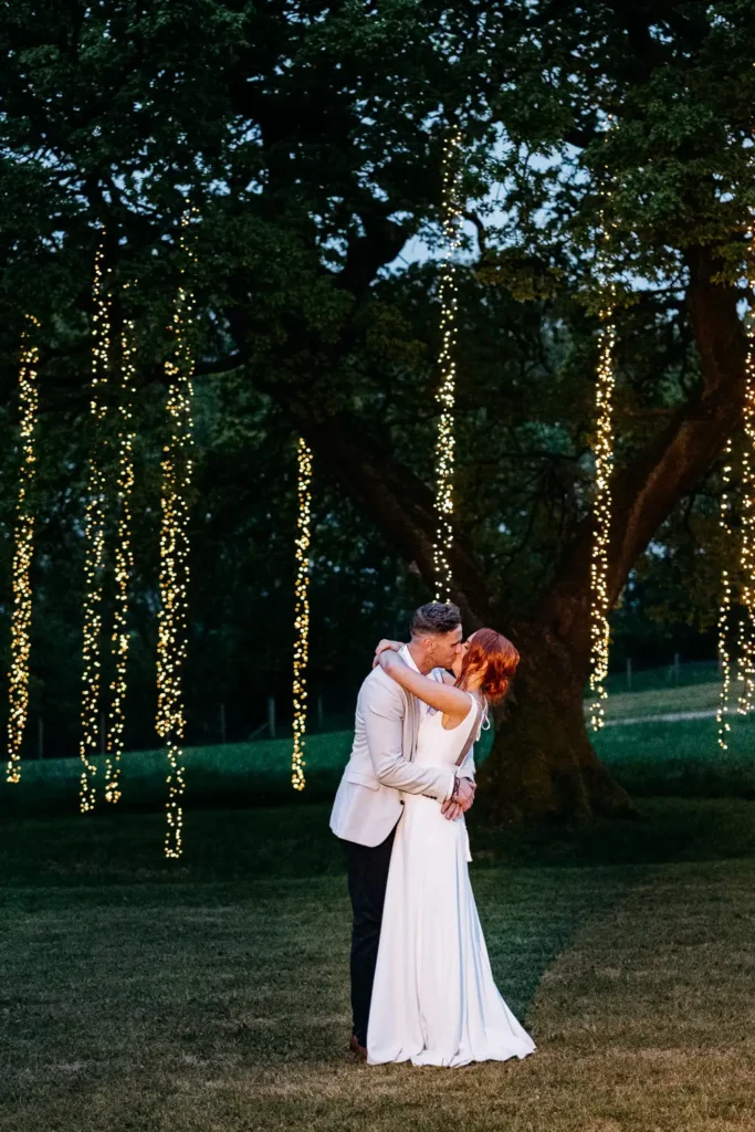 a wedding couple kissing under a lit up tree at their tipi wedding in Lancashire